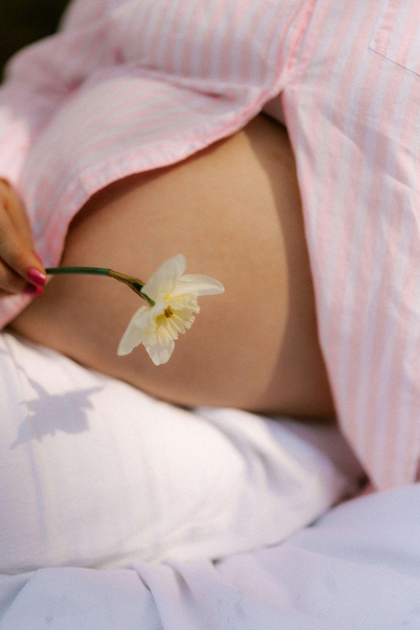 A pregnant woman holds a flower against her belly, reflecting the self-care benefits of prenatal massage near me.